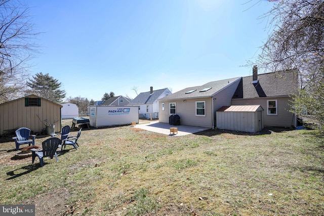 back of property with a storage unit, a patio, an outdoor fire pit, a yard, and an outdoor structure