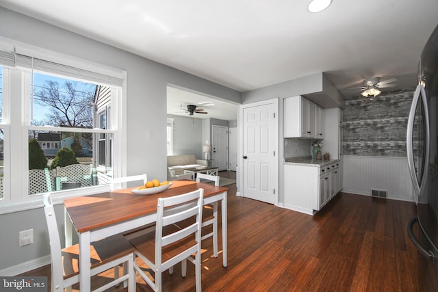 dining room with visible vents, wainscoting, baseboards, ceiling fan, and dark wood-style flooring