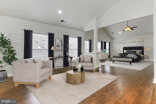 living area featuring high vaulted ceiling, visible vents, a ceiling fan, hardwood / wood-style floors, and decorative columns