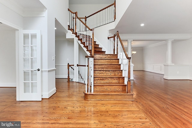 stairs featuring wood finished floors, decorative columns, and crown molding