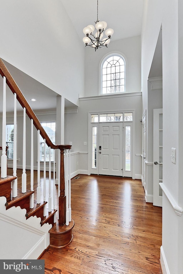 foyer entrance with stairway, an inviting chandelier, wood finished floors, and a healthy amount of sunlight