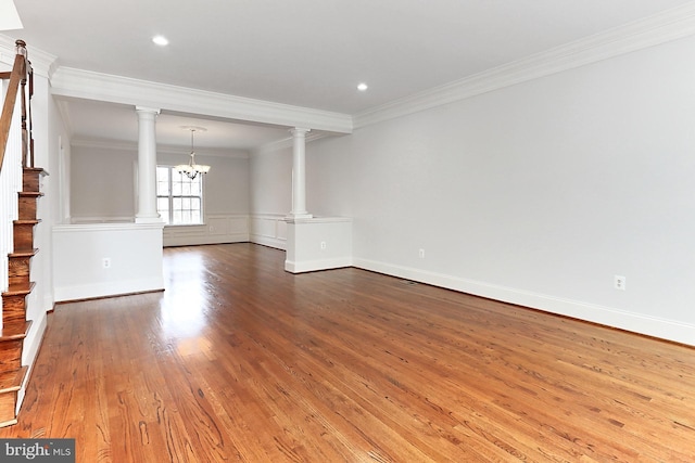 unfurnished living room with wood finished floors, ornamental molding, stairway, decorative columns, and an inviting chandelier