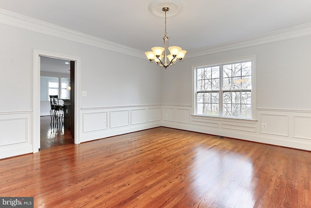 empty room with ornamental molding, wood finished floors, and a notable chandelier