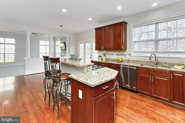 kitchen featuring decorative columns, dishwasher, a kitchen island, a breakfast bar, and a sink