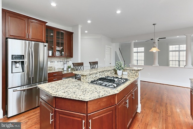 kitchen featuring light wood-style floors, a center island, light stone countertops, stainless steel appliances, and ornate columns