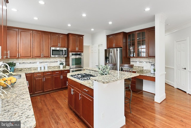 kitchen featuring light stone counters, light wood-style flooring, appliances with stainless steel finishes, a sink, and a kitchen breakfast bar