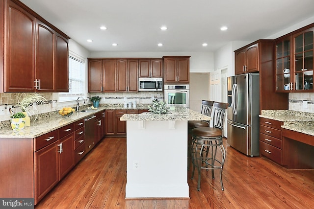 kitchen featuring a breakfast bar, a kitchen island, wood finished floors, appliances with stainless steel finishes, and glass insert cabinets