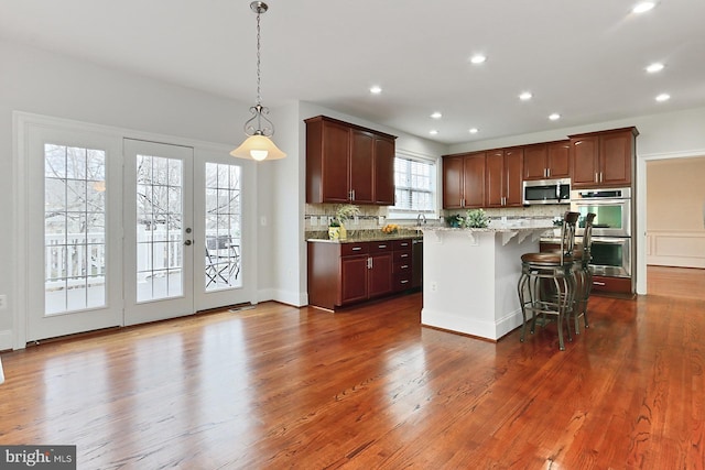 kitchen featuring tasteful backsplash, dark wood finished floors, appliances with stainless steel finishes, a kitchen breakfast bar, and a center island