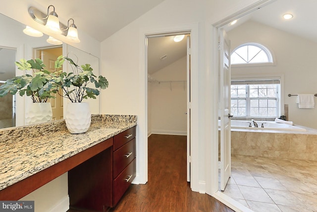 bathroom with lofted ceiling, wood finished floors, vanity, and a bath