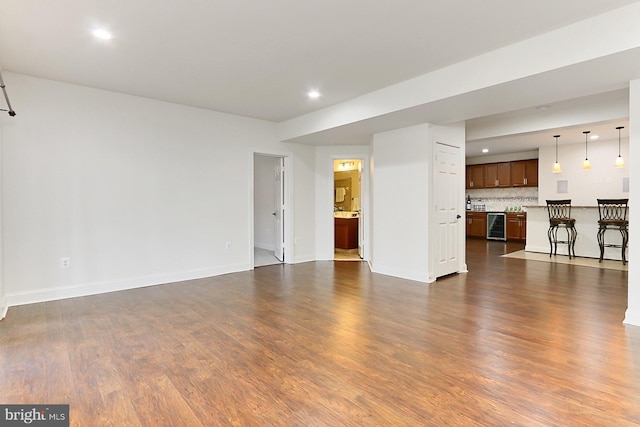 unfurnished living room featuring baseboards, wine cooler, dark wood-style flooring, and recessed lighting