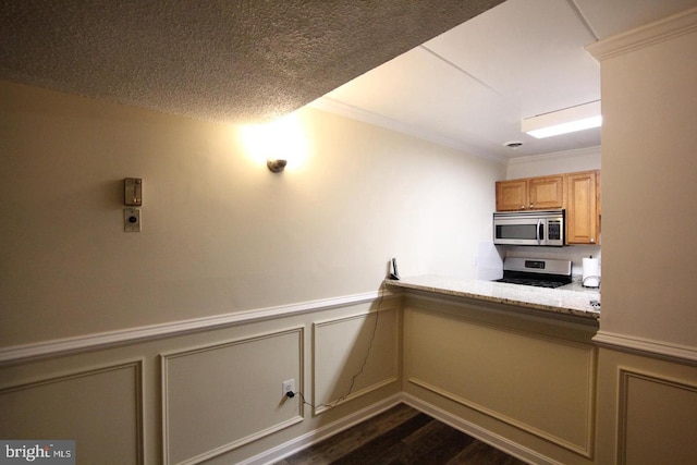 kitchen featuring crown molding, appliances with stainless steel finishes, dark wood-type flooring, wainscoting, and a textured ceiling