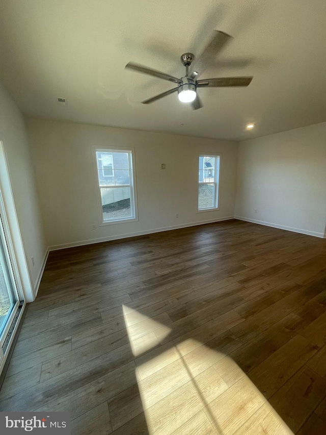 unfurnished room with visible vents, dark wood-style flooring, a ceiling fan, and baseboards