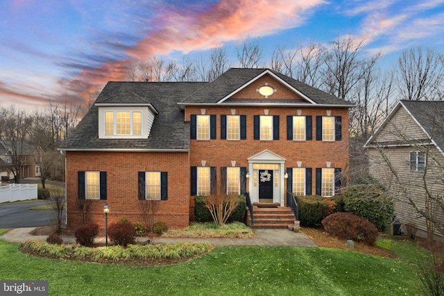 view of front of property with roof with shingles, brick siding, and a lawn