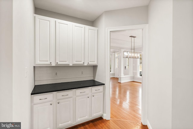 interior space with dark countertops, backsplash, light wood-style flooring, white cabinetry, and baseboards