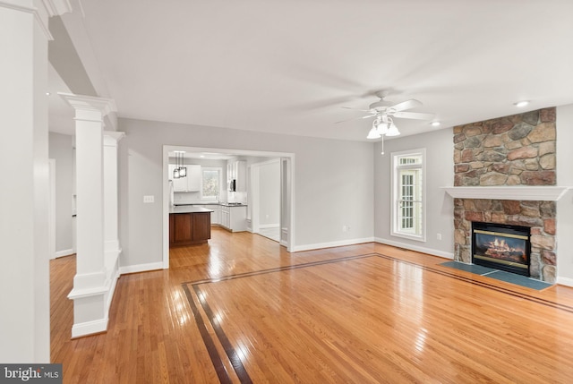 unfurnished living room featuring a fireplace, decorative columns, a ceiling fan, light wood-type flooring, and baseboards