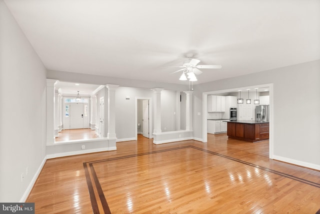 unfurnished living room with light wood-type flooring, decorative columns, and baseboards