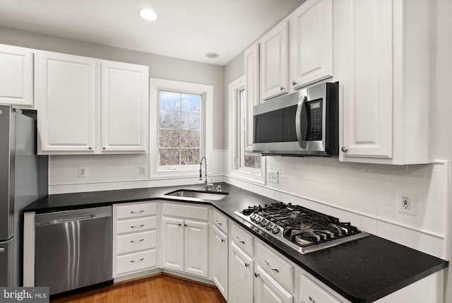 kitchen featuring dark countertops, appliances with stainless steel finishes, a sink, white cabinetry, and backsplash