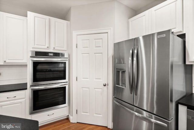 kitchen with dark countertops, white cabinets, stainless steel appliances, and wood finished floors