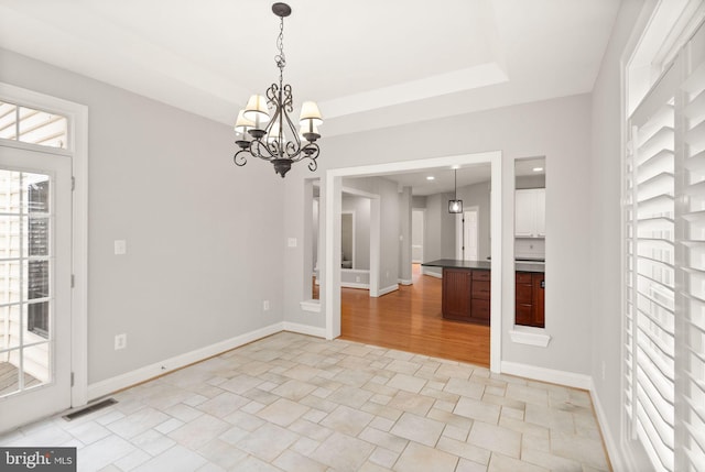 unfurnished dining area with an inviting chandelier, a raised ceiling, visible vents, and baseboards