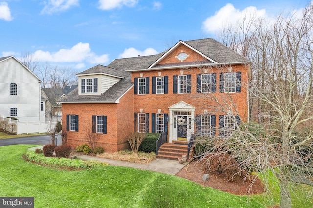 view of front of house featuring brick siding, a front lawn, and roof with shingles