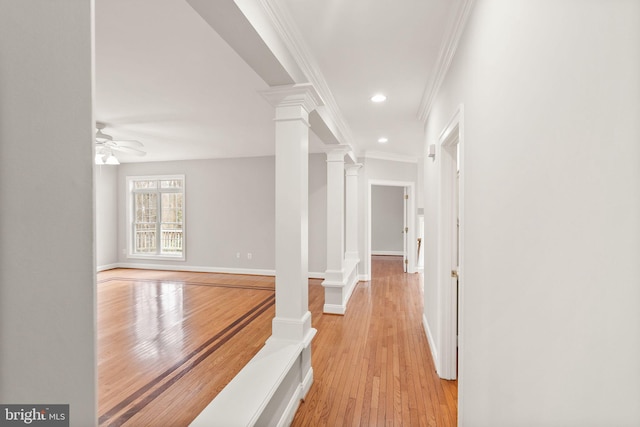 corridor featuring light wood-style flooring, recessed lighting, baseboards, decorative columns, and crown molding