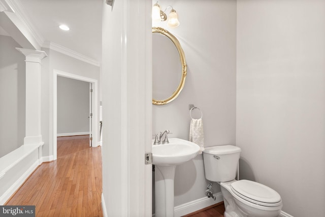 bathroom with decorative columns, toilet, ornamental molding, wood finished floors, and baseboards