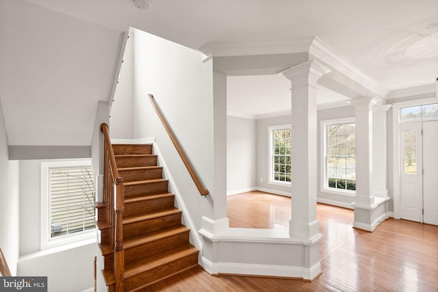 stairs featuring decorative columns, ornamental molding, and wood finished floors