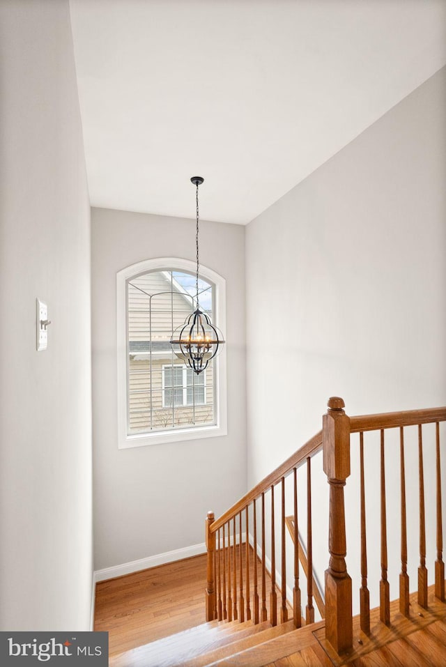 stairs with a notable chandelier, baseboards, and wood finished floors