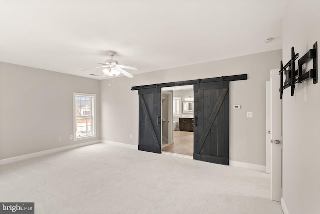 unfurnished bedroom featuring a barn door, a ceiling fan, baseboards, carpet, and ensuite bath