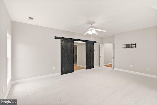 unfurnished bedroom with a barn door, visible vents, baseboards, a ceiling fan, and carpet floors