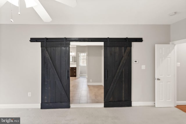 unfurnished bedroom with carpet floors, a barn door, a ceiling fan, and baseboards