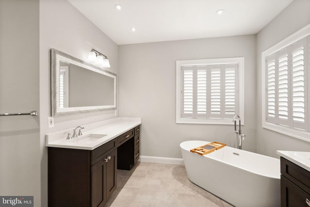 bathroom with recessed lighting, a freestanding tub, vanity, and baseboards