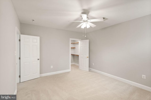 unfurnished bedroom with baseboards, a ceiling fan, light colored carpet, a spacious closet, and a closet