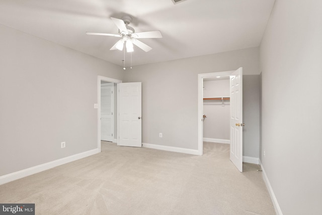 unfurnished bedroom featuring baseboards, a closet, a walk in closet, and light colored carpet