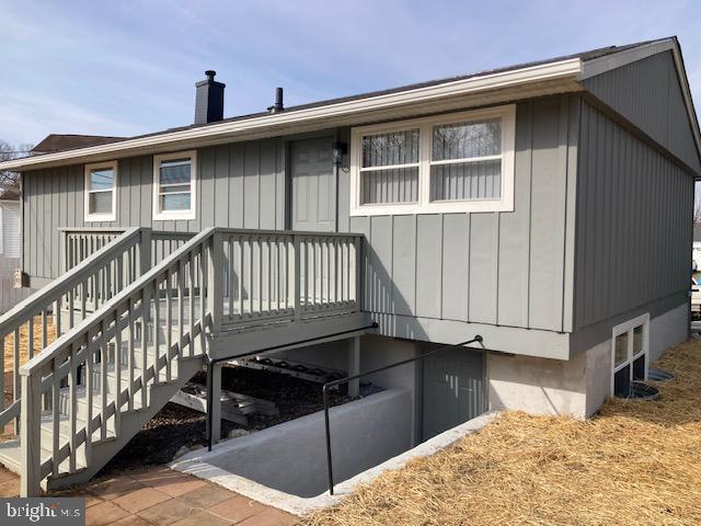 back of property featuring board and batten siding, a chimney, and stairs