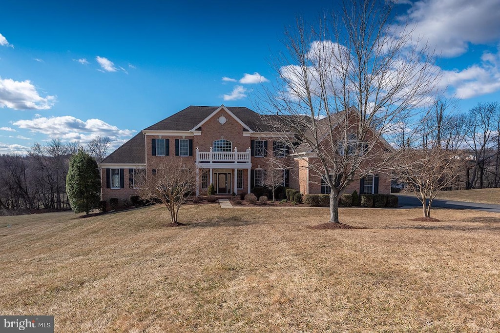 view of front facade with a front yard, brick siding, and a balcony