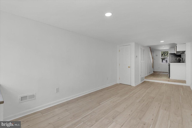 unfurnished living room with light wood finished floors, recessed lighting, visible vents, a sink, and baseboards