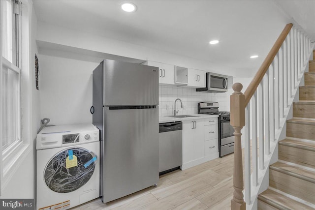 kitchen featuring light wood-style flooring, stainless steel appliances, white cabinetry, light countertops, and washer / clothes dryer