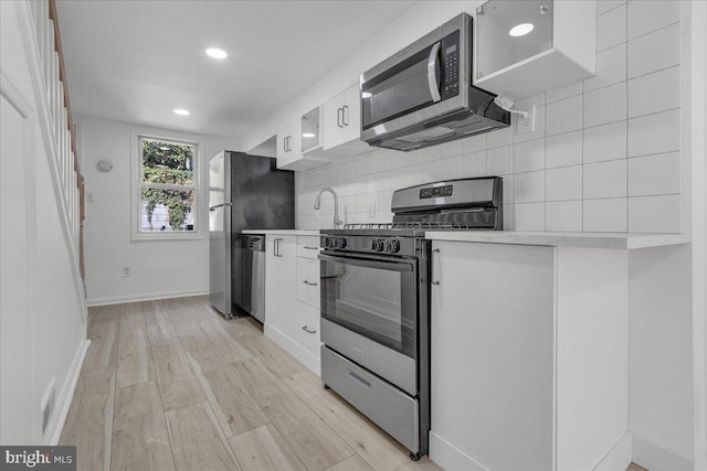 kitchen with light wood finished floors, light countertops, backsplash, appliances with stainless steel finishes, and white cabinetry