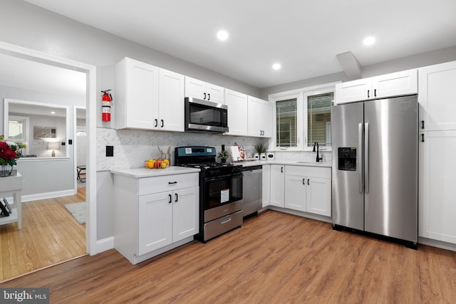 kitchen with light wood finished floors, light countertops, decorative backsplash, appliances with stainless steel finishes, and white cabinetry