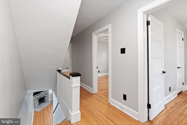 hall with baseboards, light wood-style flooring, and an upstairs landing