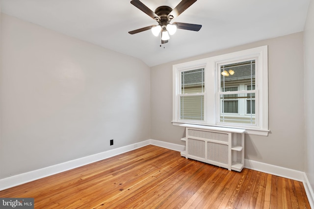 spare room featuring radiator, light wood-style flooring, baseboards, and a ceiling fan