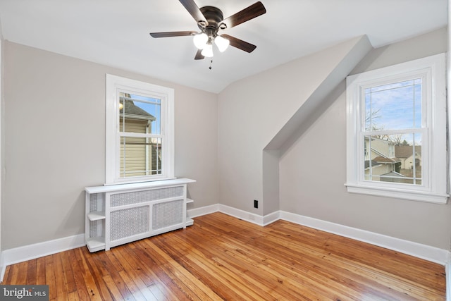 additional living space featuring radiator, wood-type flooring, baseboards, and ceiling fan