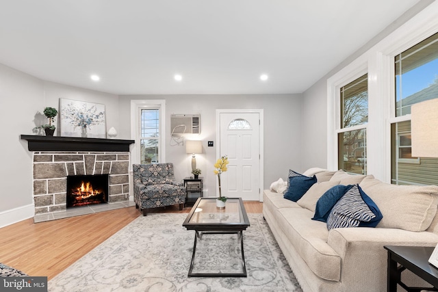 living room with a wall unit AC, recessed lighting, wood finished floors, and a stone fireplace