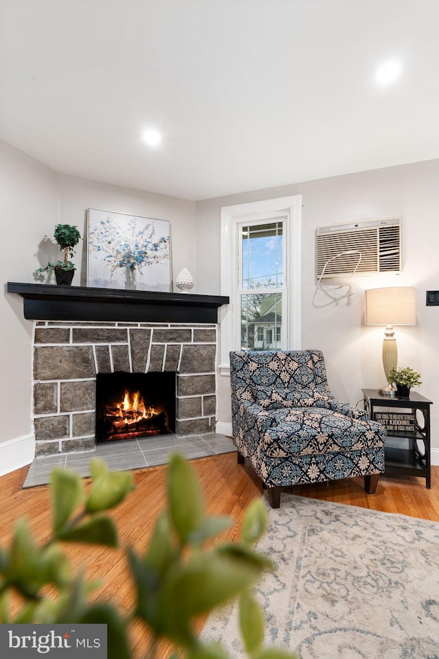 living area featuring an AC wall unit, a fireplace, wood finished floors, and baseboards