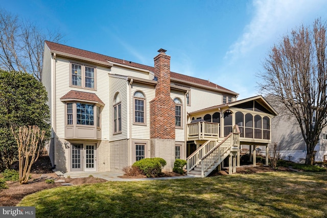 back of property featuring a sunroom, stairs, a chimney, and a lawn