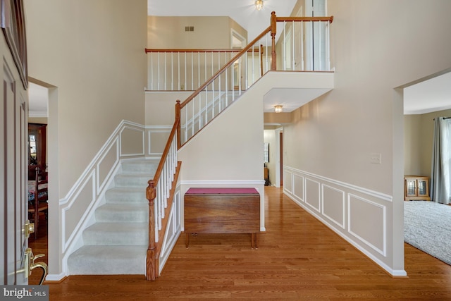 stairs featuring a wainscoted wall, a high ceiling, a decorative wall, and wood finished floors