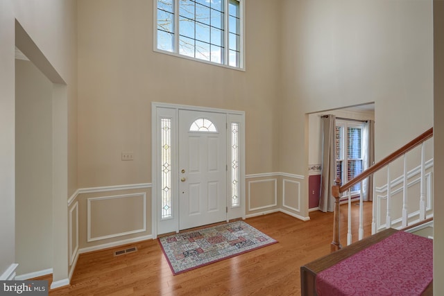 foyer with a decorative wall, wood finished floors, a towering ceiling, visible vents, and stairs