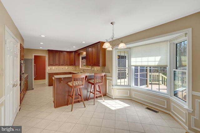 kitchen with a peninsula, light tile patterned floors, tasteful backsplash, and visible vents