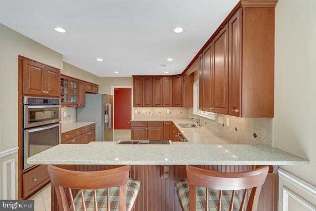 kitchen featuring a peninsula, appliances with stainless steel finishes, decorative backsplash, light stone countertops, and glass insert cabinets